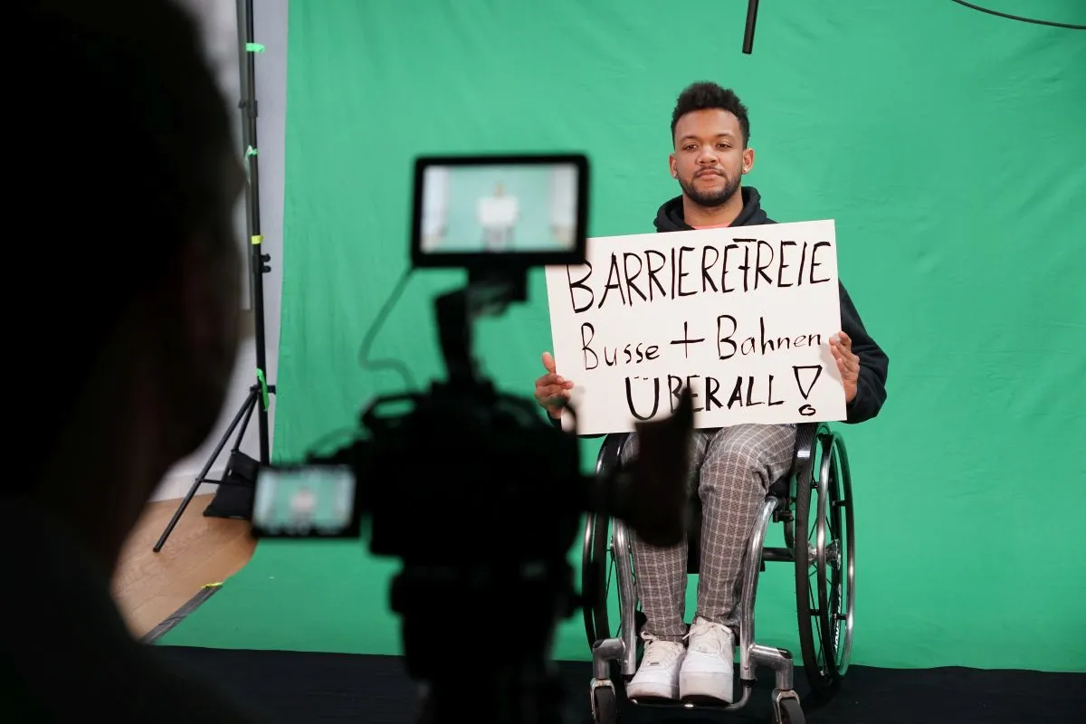 Leeroy Matata sitzt am Greenscreen-Set mit einer Forderung zum 5. Mai