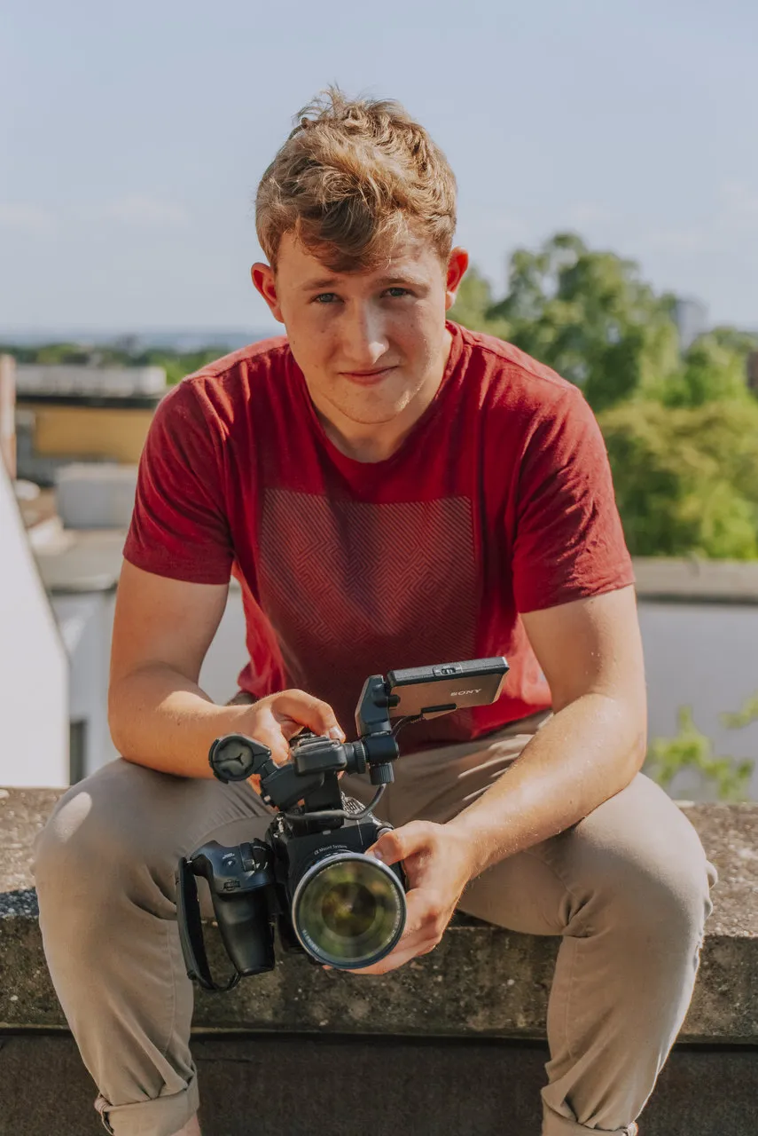 Felix sitzt in der Sonne mit einer Kamera in der Hand