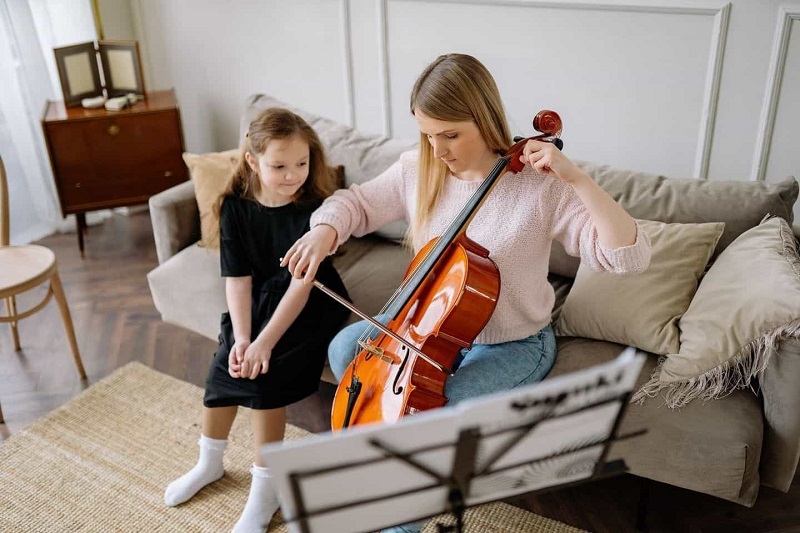 A Girl Wearing Black Top Siting on Sofa At Home Watching A Woman Playing Violin Besides Her