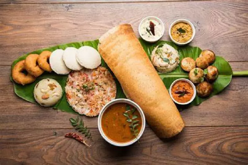 South indian food is kept on the banana leaf placed on the brown surface