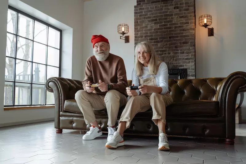 A old man and a women is sitting on a sofa playing video game