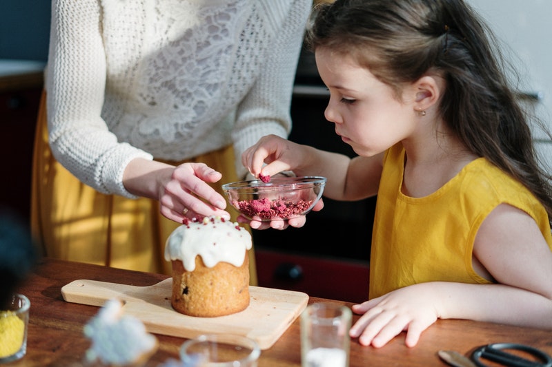 A girl decorating cake with the help of a women.