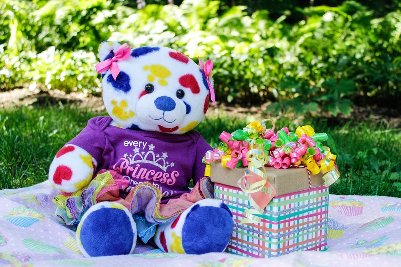 A Colorful Teddy Bear Sitting on Carpet in Garden With Decorative Gift Box
