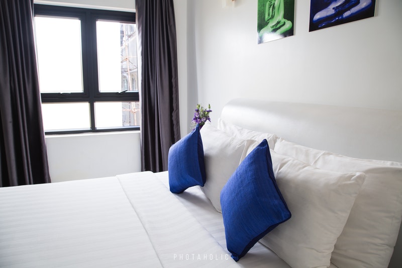 A Double Bed With White Mattresses and Blue & White Cushion With Window View