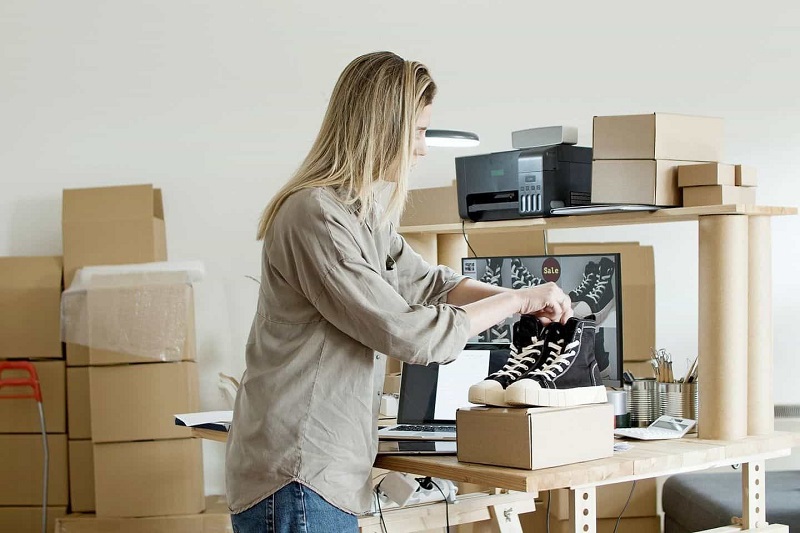 A women is packing black shoes in the brown box.