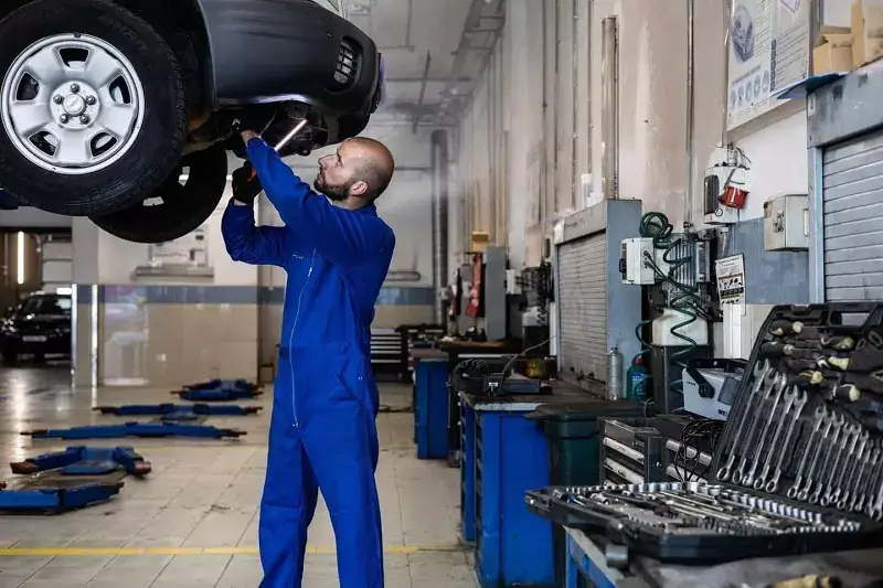 A Service Man is Repairing A Car in A Garage.