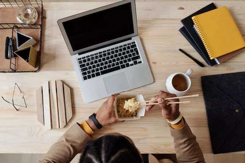 A lady eating ramen on the table front of laptop