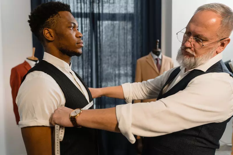A tailor is taking measure of his client