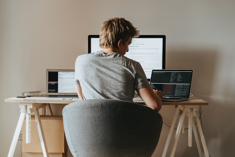 A boy working in his laptop sitting on the desk.