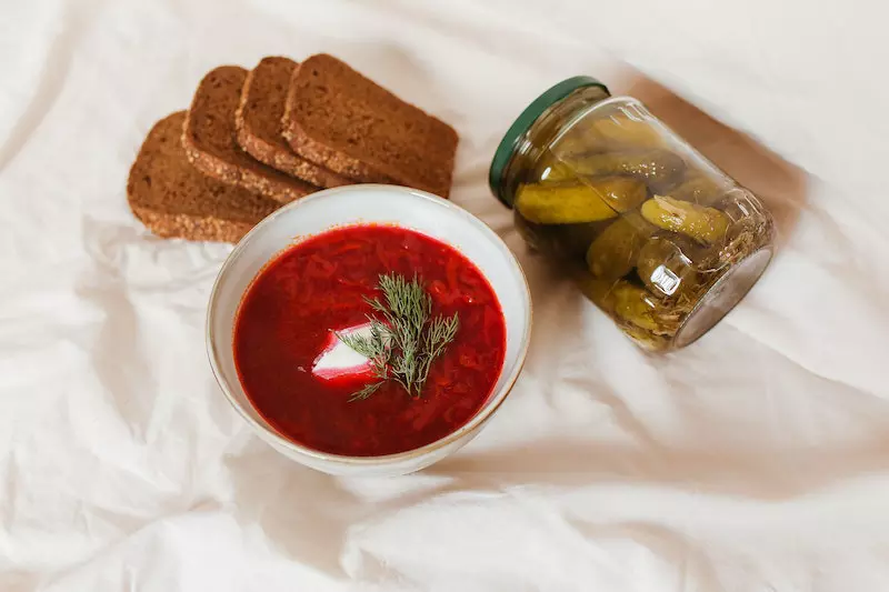 A jar of dill pickles and a bowl of food is placed on the bed