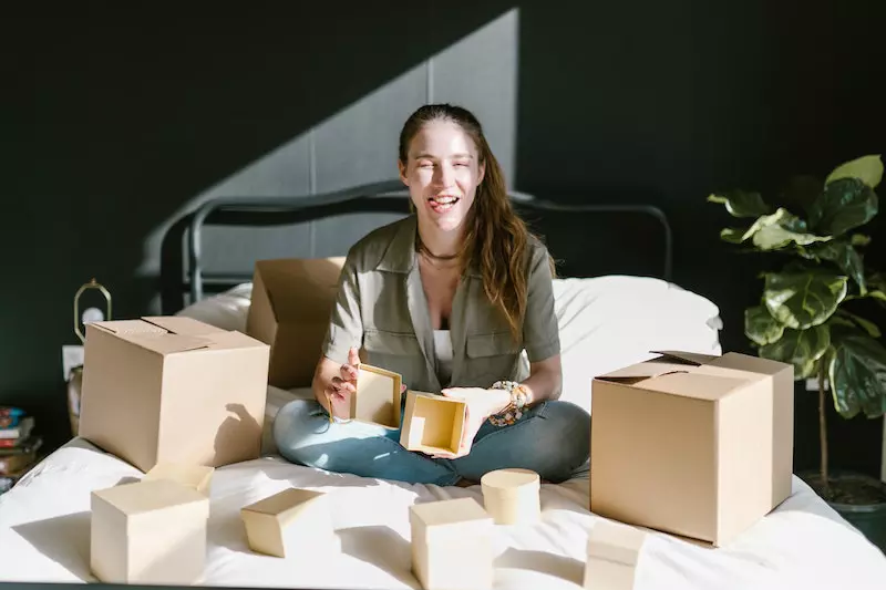 A girl is sitting on the bed holding a empty box in her hand 