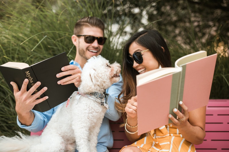 A man and a women is sitting on a bench with pet dog.