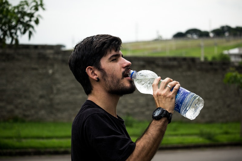 A man is drinking water from the bottle. 