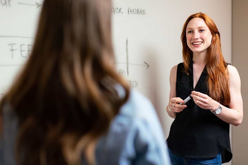 A women guiding a girl with the help of a whiteboard.