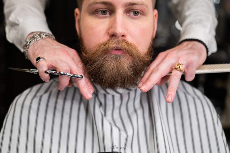 A barber is cutting beard of a man.
