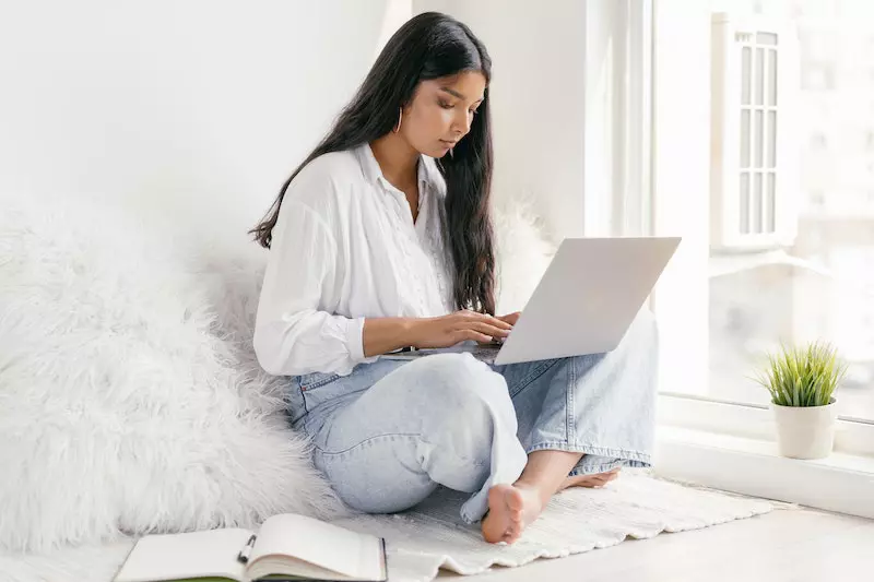 A Lady  using laptop in the bed and write on the book