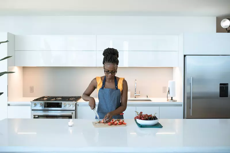 A lady is cutting vegetable standing in the kitchen
