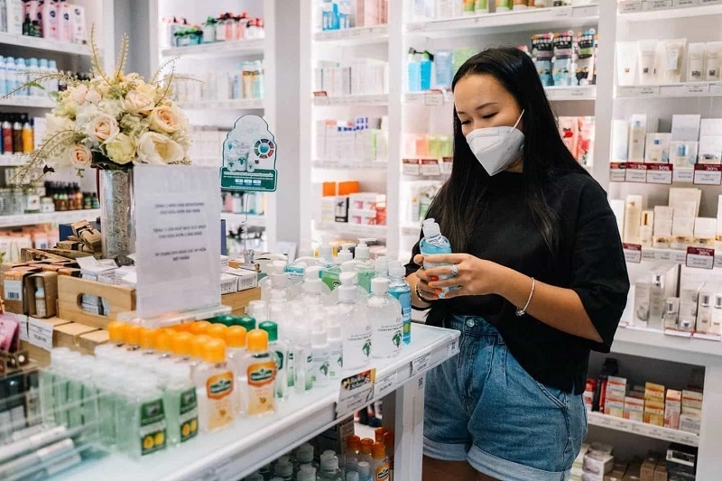 A lady is standing at a medical store holding a bootle in her hand