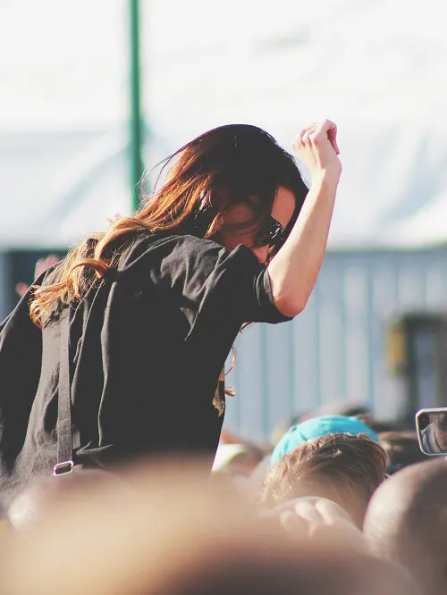 Woman with long hair and sunglasses raising her fist above a crowd at an outdoor event.