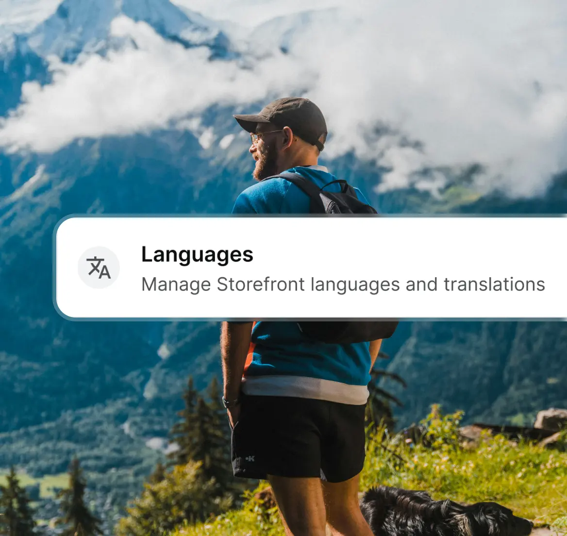 Man with backpack and a dog hiking in a mountainous landscape with clouds.