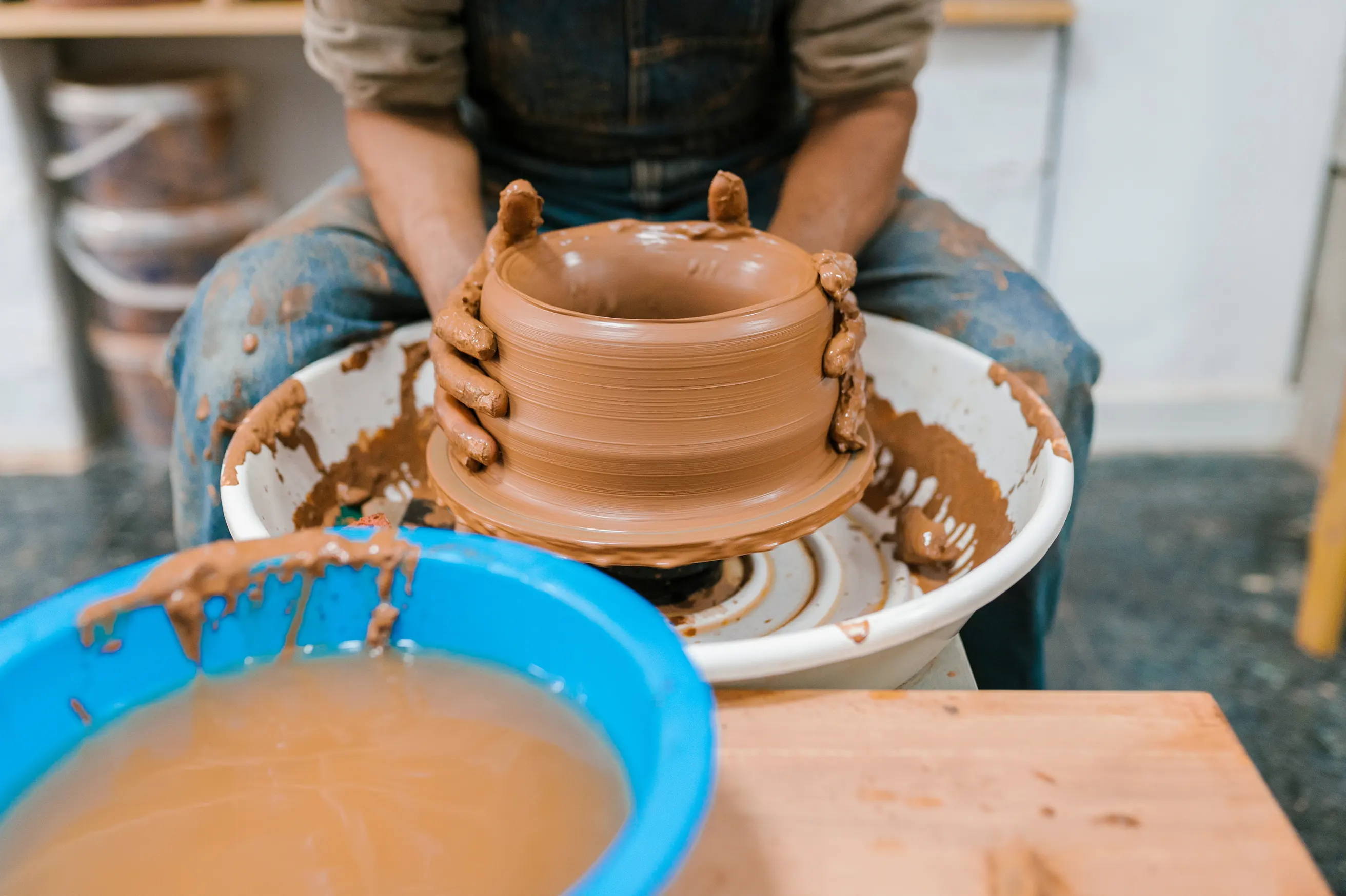 Close-up of a potter shaping a clay pot on a spinning pottery wheel with muddy hands.
