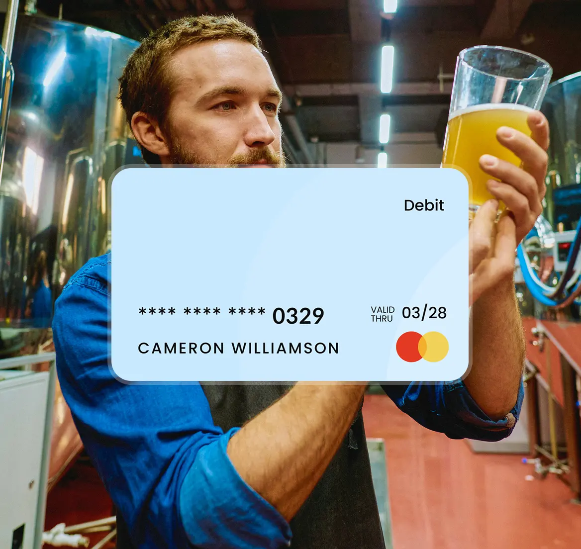 Man in blue shirt examining a glass of beer in a brewery with a Mastercard debit card graphic overlay.