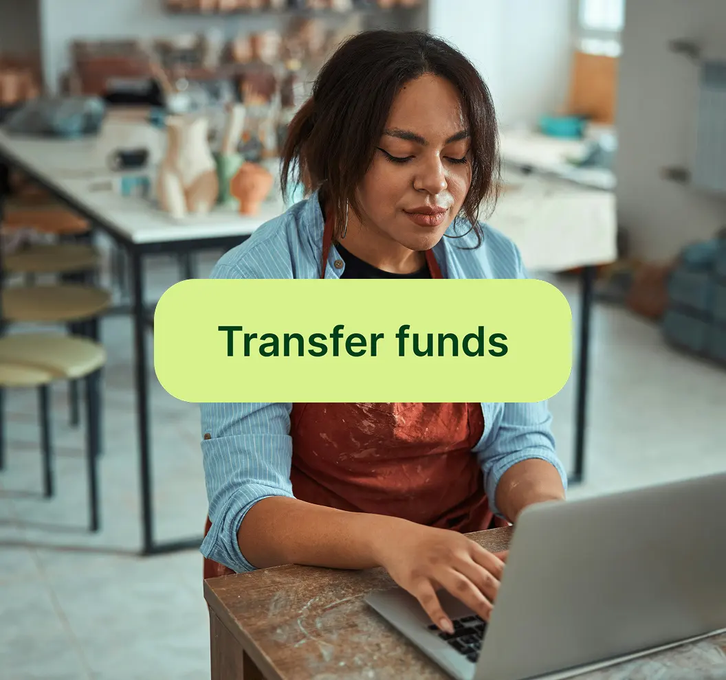 Woman in an apron working on a laptop in a pottery studio with various clay sculptures in the background.
