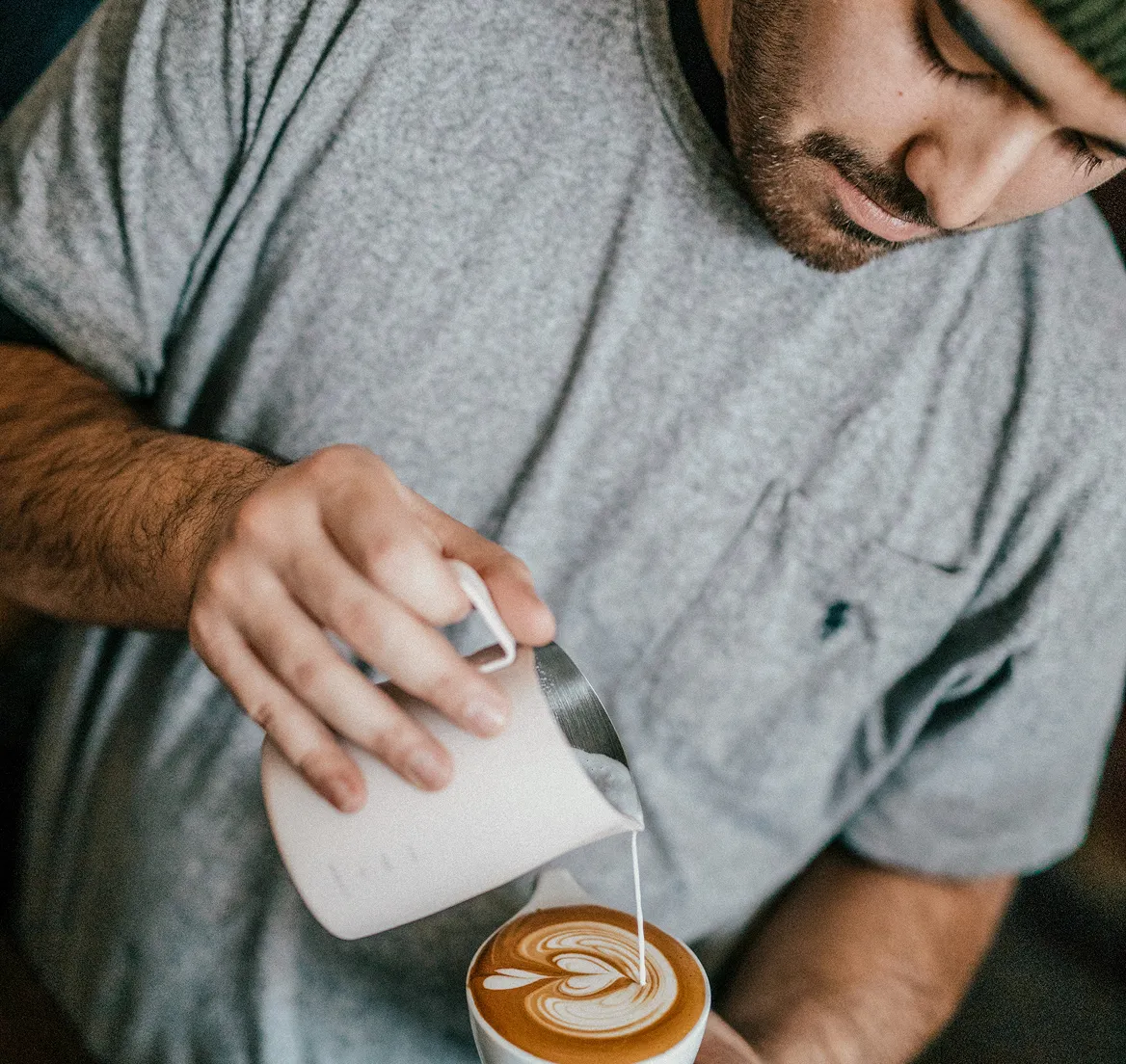 Barista pouring milk to create latte art in a cup of coffee.