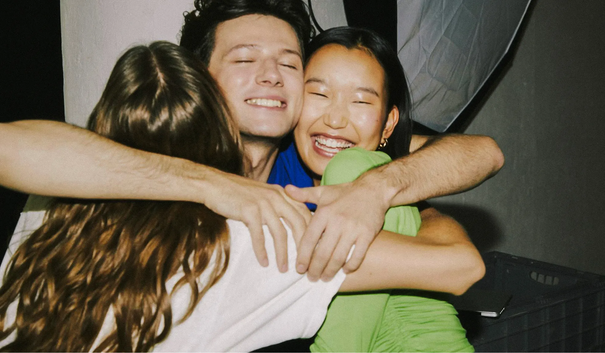 Three friends joyfully hugging each other with smiling faces in a warm embrace.
