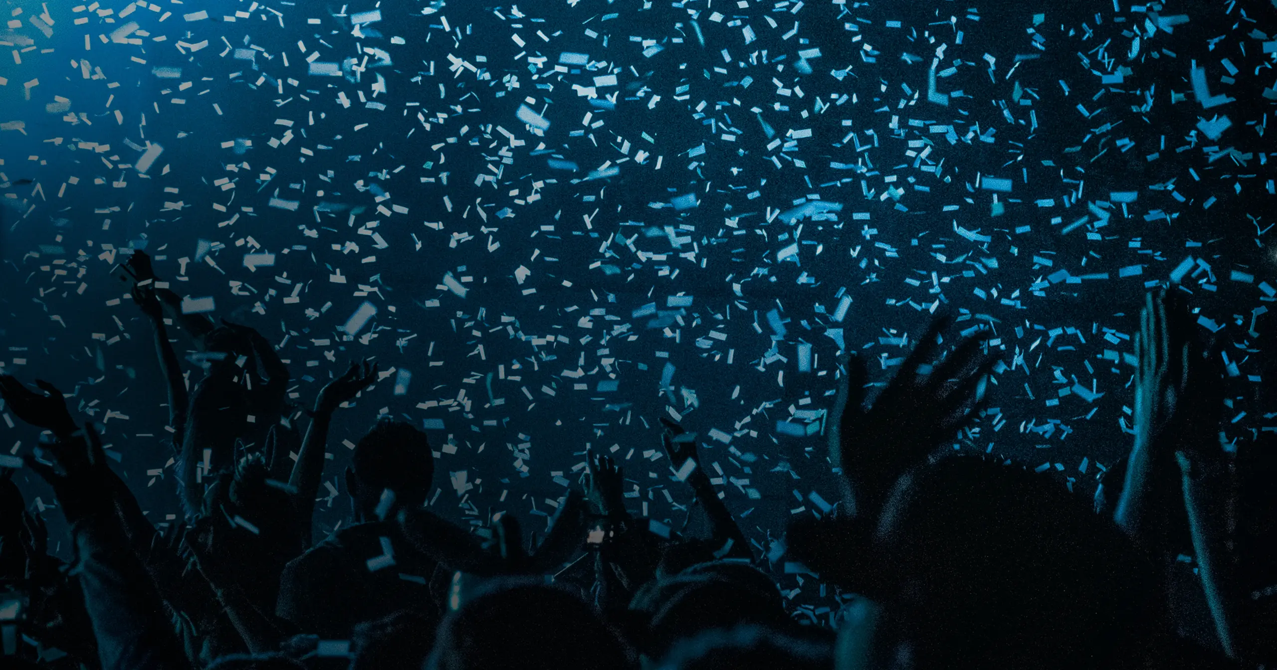 Silhouetted crowd with raised hands under falling confetti in blue lighting at a celebration or concert.