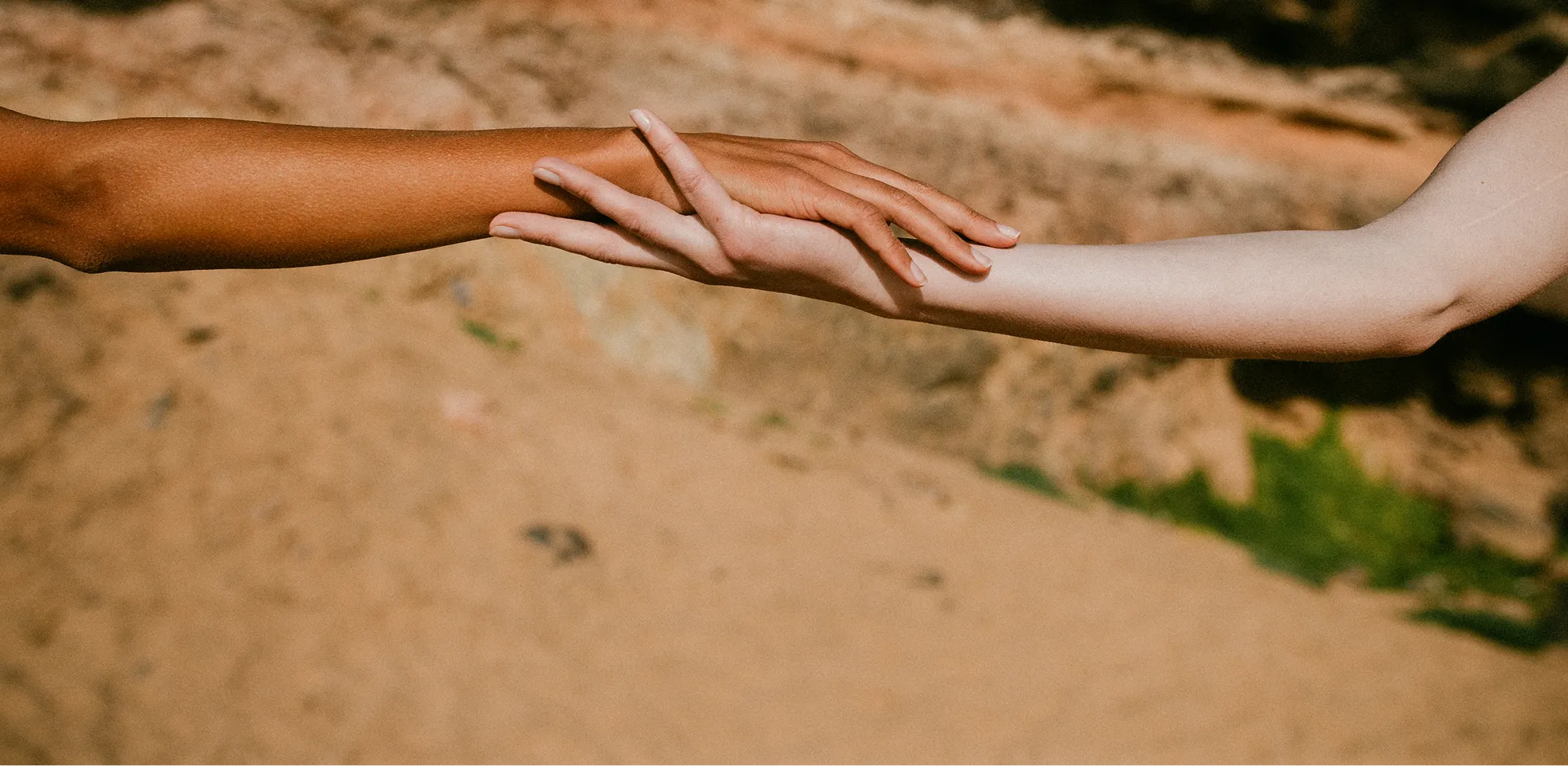 Two arms of different skin tones reaching toward each other with fingers gently touching.