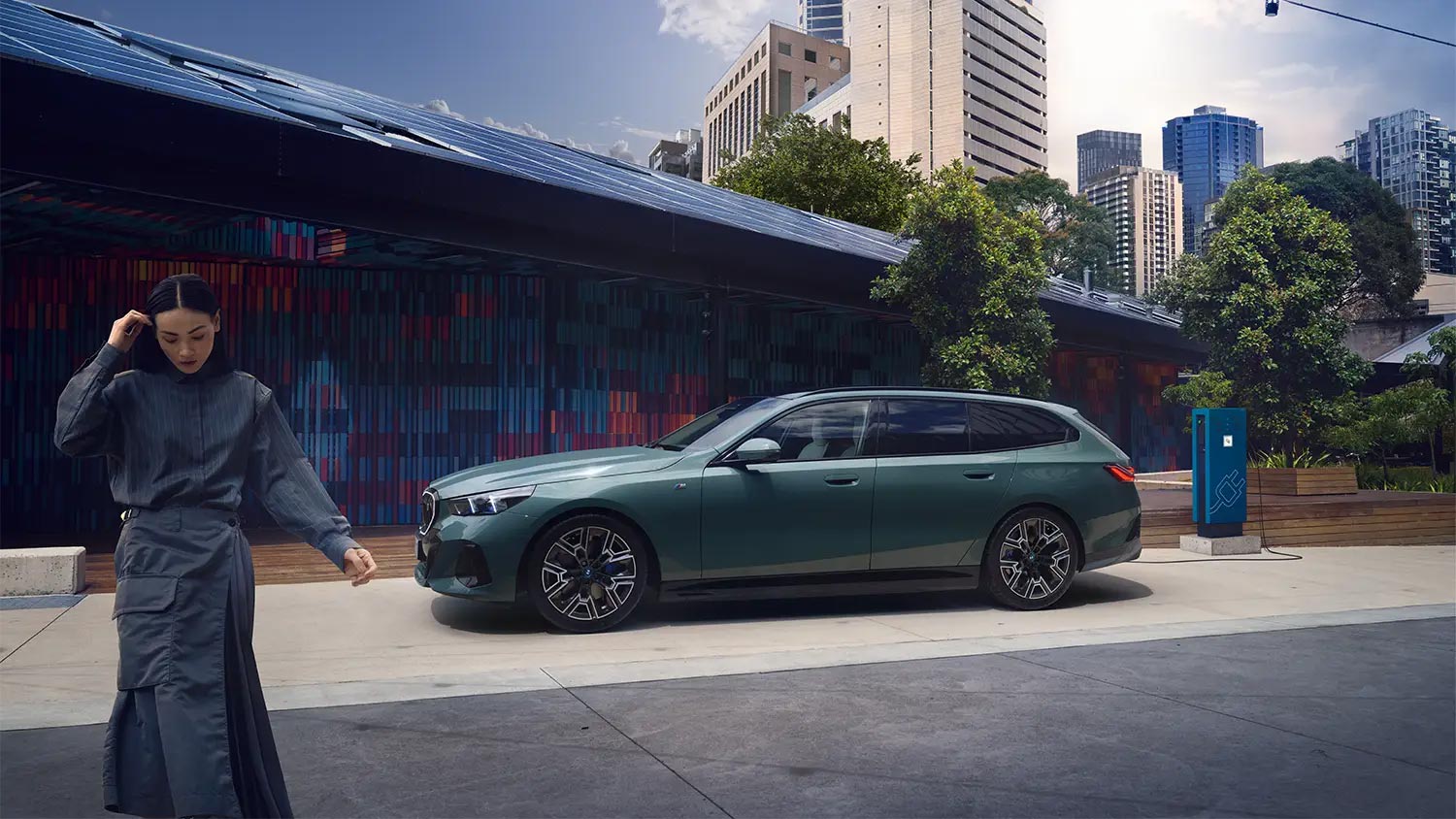 BMW 5er Touring Plug-in-Hybrid in mattem Grün vor moderner Stadtkulisse mit Solardach – BMW Köhler in Karlstadt