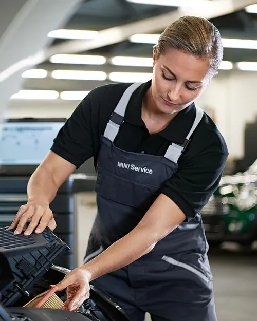 Servicemitarbeiterin reinigt die Front eines MINI mit einem Tuch – MOTORHEIMAT Wagner-Schwarz in Kirchseeon, Traunstein, Altenmarkt, Wasserburg und Oberhaching
