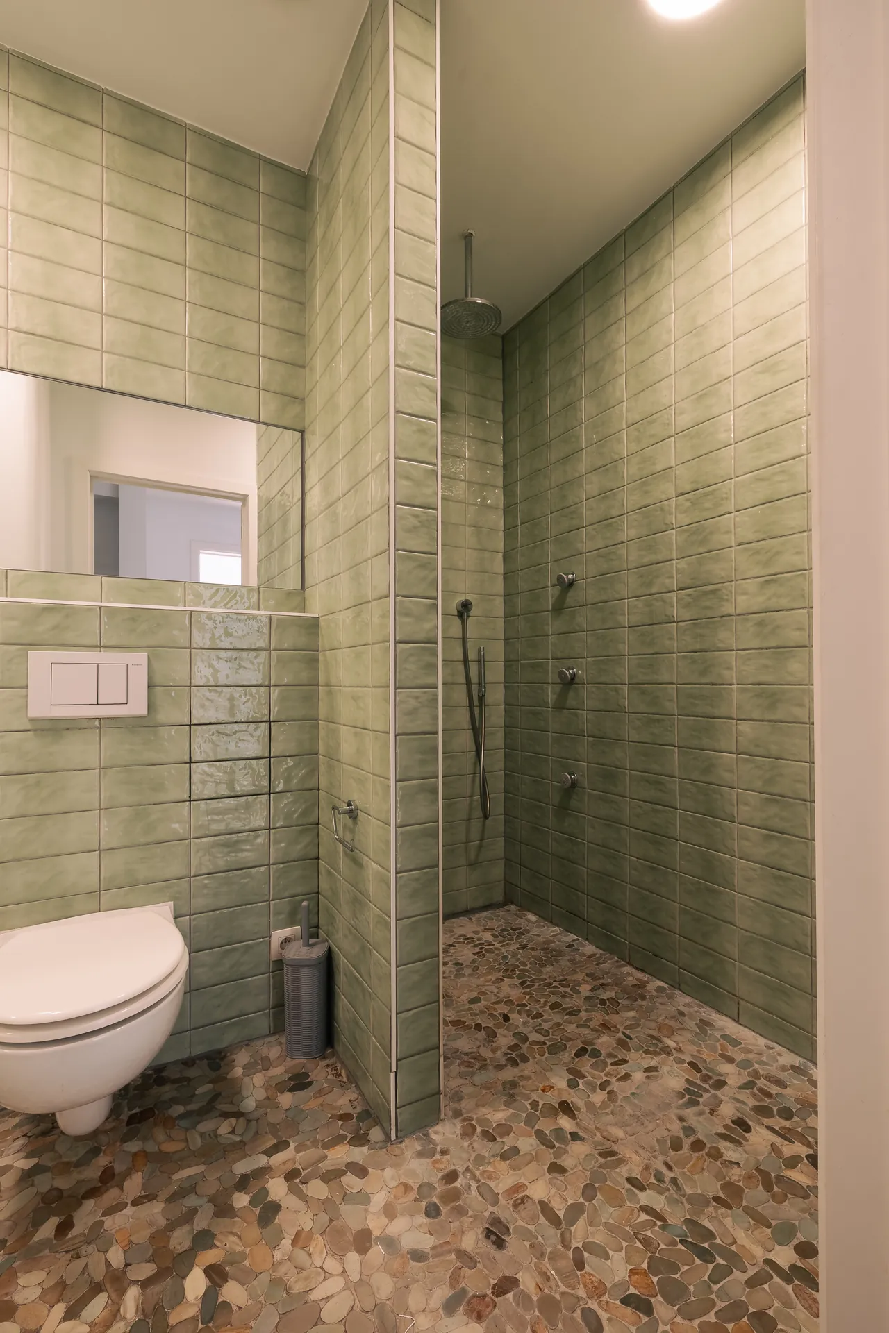 Salle de douche : carrelage vert en relief, sol en galets, WC suspendu — maison rénovée à Saint-Gilles, Bruxelles
