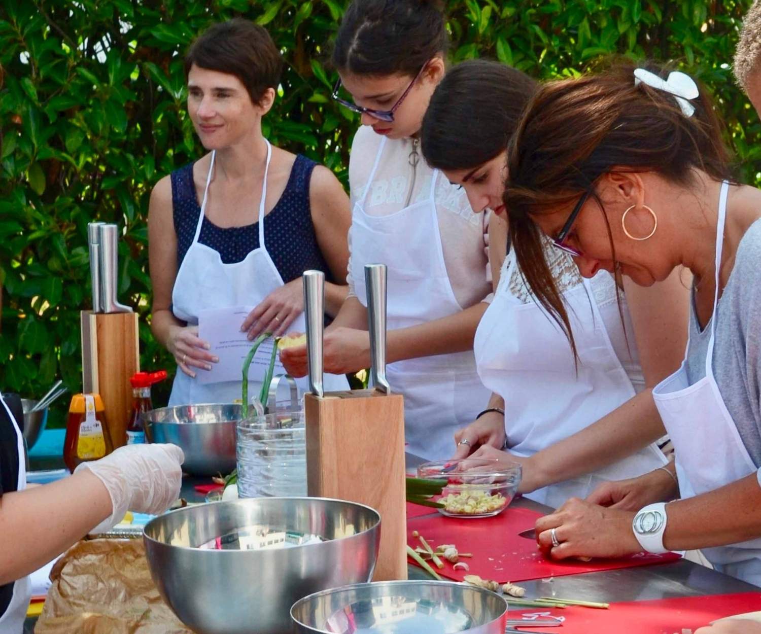 Groupe de femmes participant à un atelier de cuisine en plein air, concentrées sur la préparation des ingrédients, dans une ambiance conviviale et collaborative.