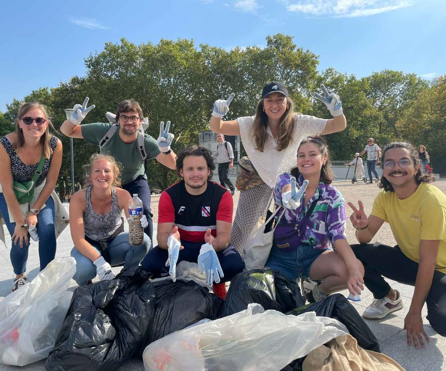 Groupe de bénévoles souriants posant autour de sacs remplis de déchets collectés lors d'une opération de nettoyage urbain. Une action collective pour l’environnement sous un ciel bleu.