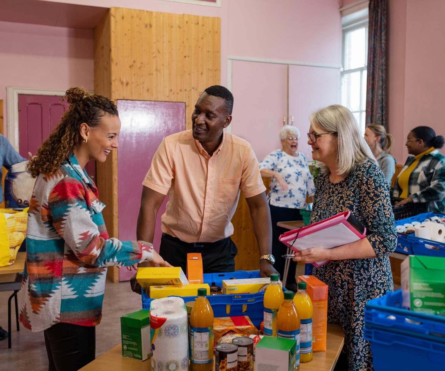 Des bénévoles échangent dans une épicerie solidaire ou une banque alimentaire, entourés de produits de première nécessité. Une scène chaleureuse d’entraide et de distribution alimentaire.