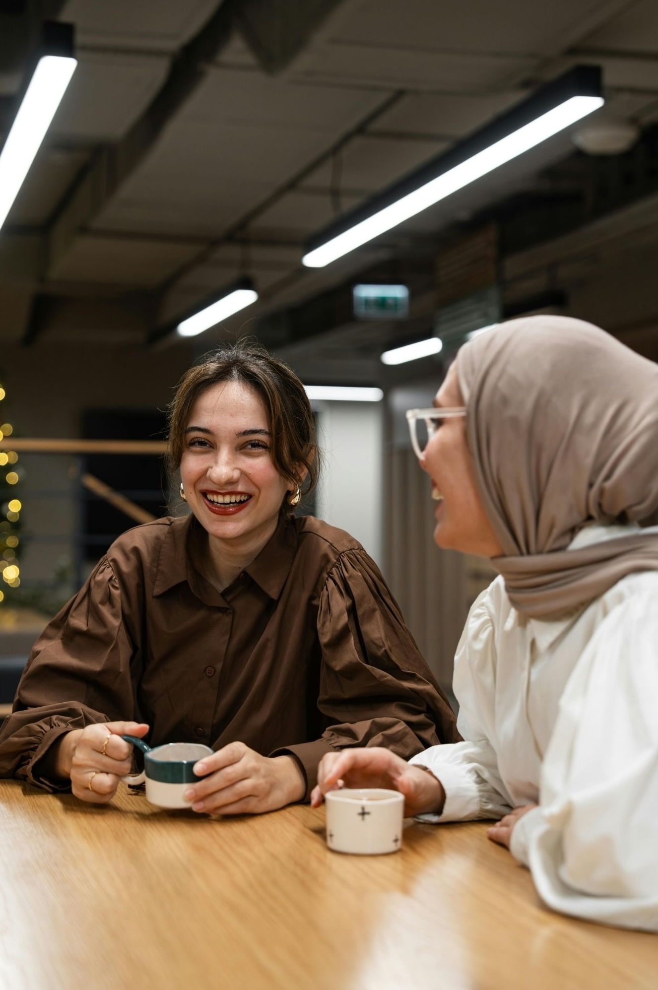 2 femmes assises autour d'une table à une pause café, souriantes et joyeuses