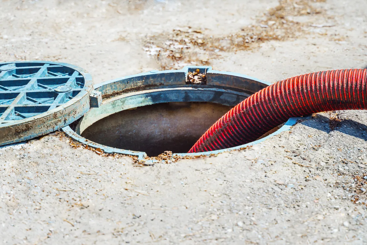 A red hose extending into an open septic tank access port.
