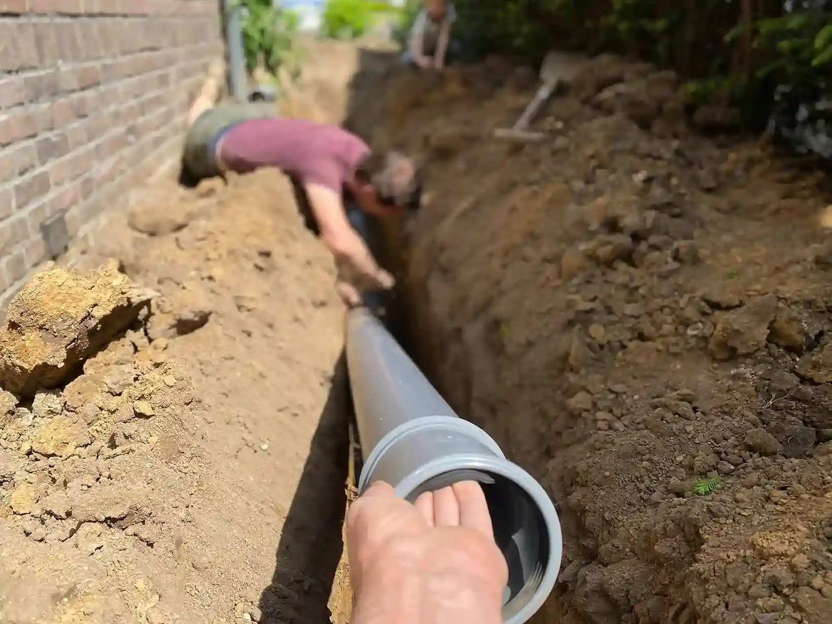 People working to install a grey sewer line in a trench.