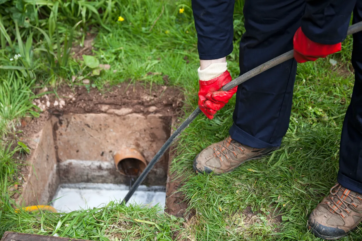Person in red gloves using a drain camera to inspect a pipe in the ground.