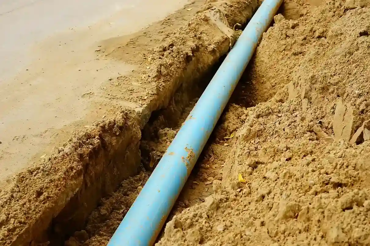A light blue pipe runs through a trench dug into dry, light brown dirt.