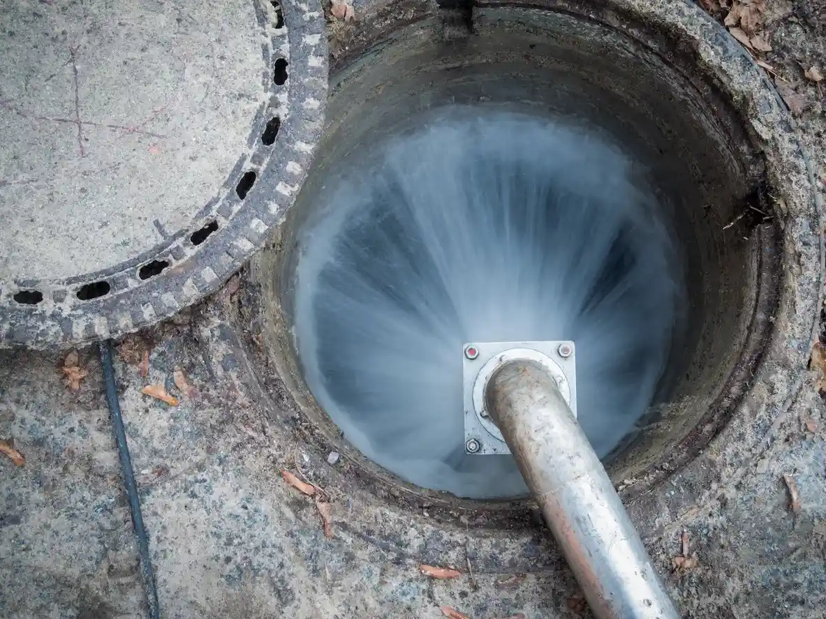 High pressure water jet cleaning a drain in an open manhole.