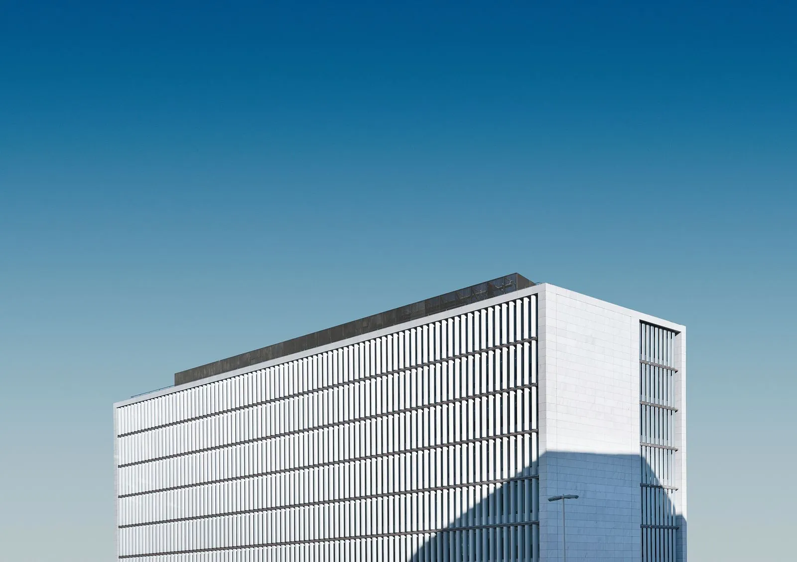 Pristine modern building with a sleek, white facade and geometric lines, standing tall against a clear blue sky, embodying minimalist elegance and contemporary design.