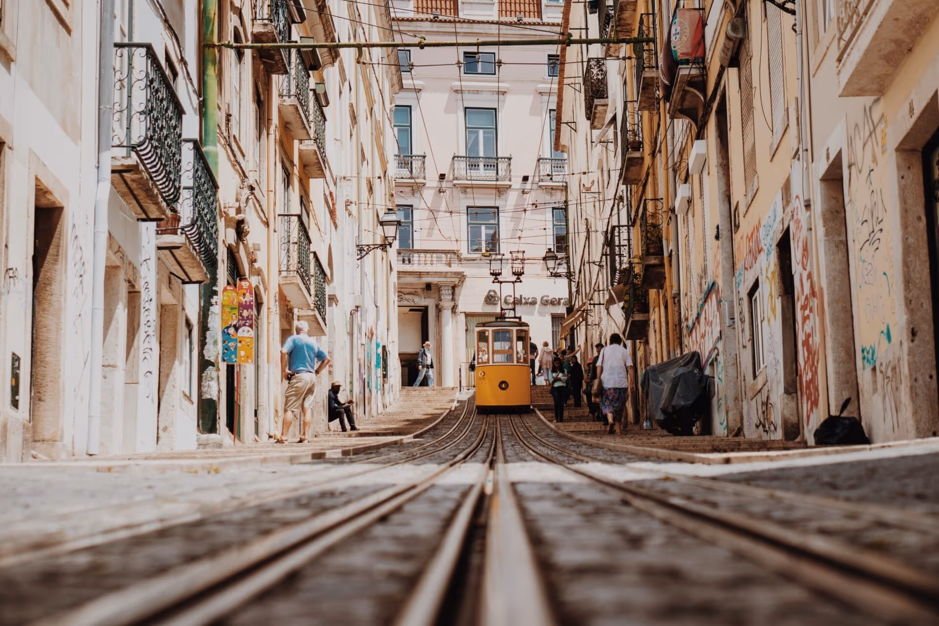 A yellow tram car is on a track in a city.