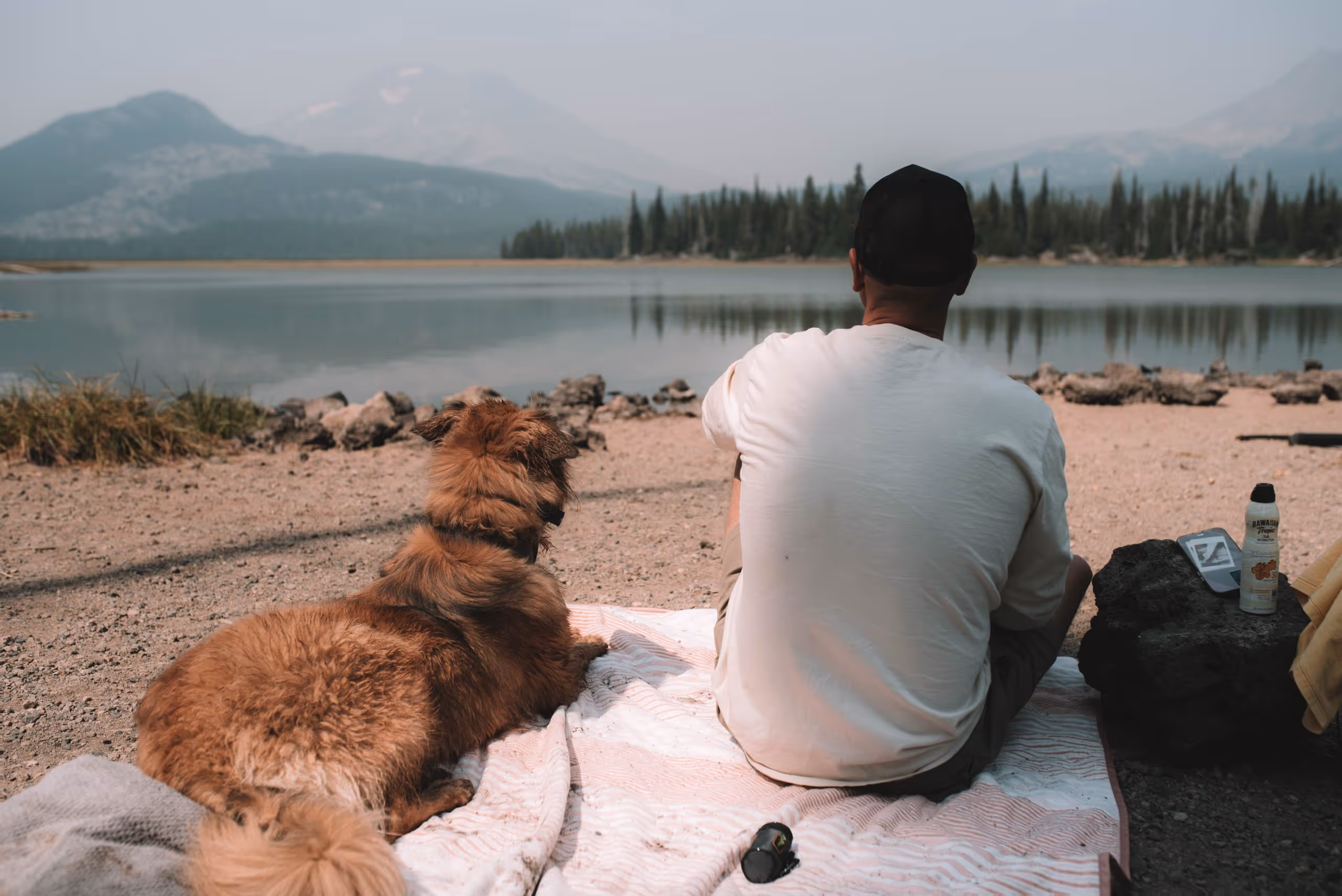 A man sitting on a blanket with his dog.