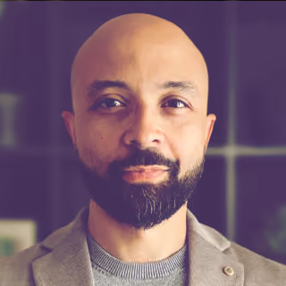 Fotografia de Mao Barros, homem careca de barba e casaco bege
