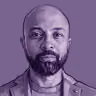 Portrait of a bald man with a beard against a purple background.