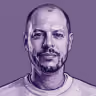 Close-up portrait of a bald man with a beard on a purple background.