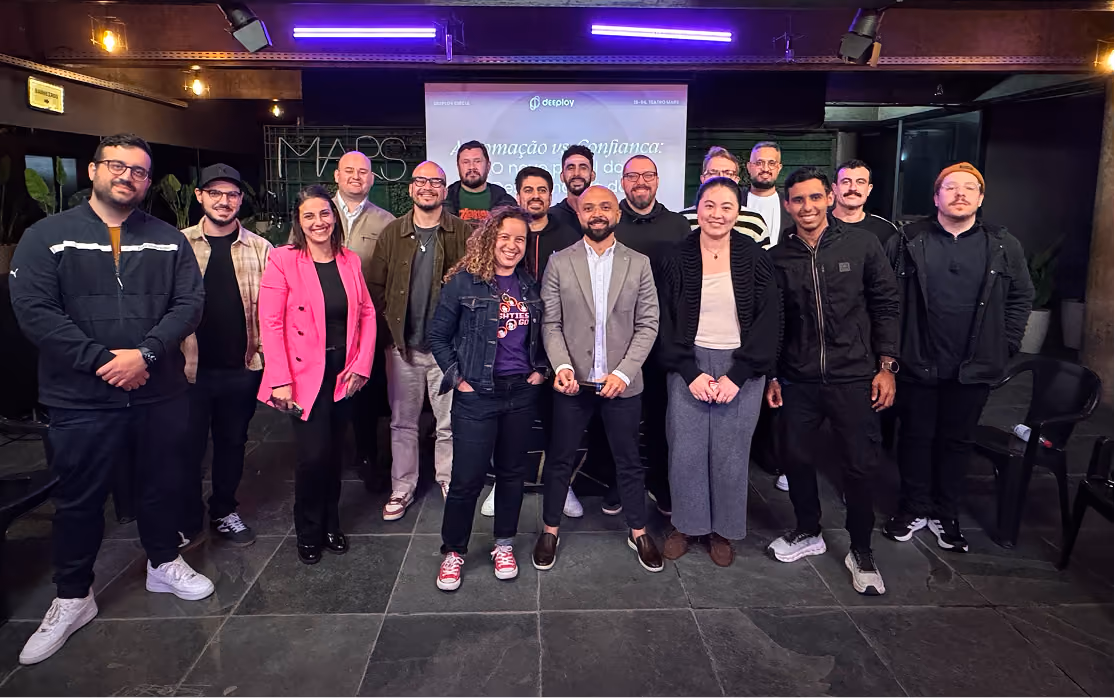 Group photo of 17 diverse adults standing indoors on a tiled floor with a presentation screen behind them showing text and a logo reading Deeploy.